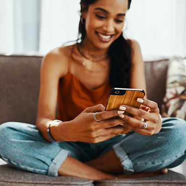 Young woman holding mobile phone at home on couch.