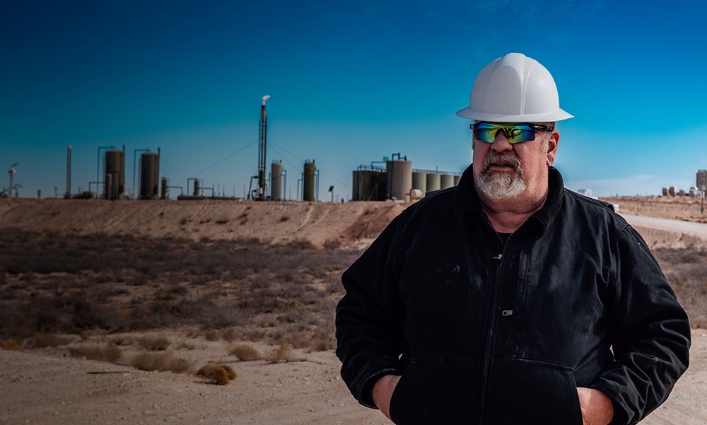 Man wearing hard hat and glasses, standing on construction site. 
