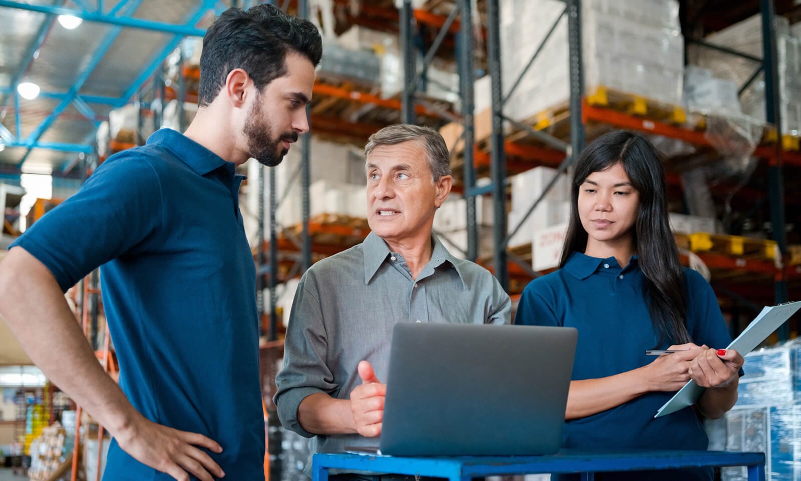 two men and a woman working on computer in a warehouse. 