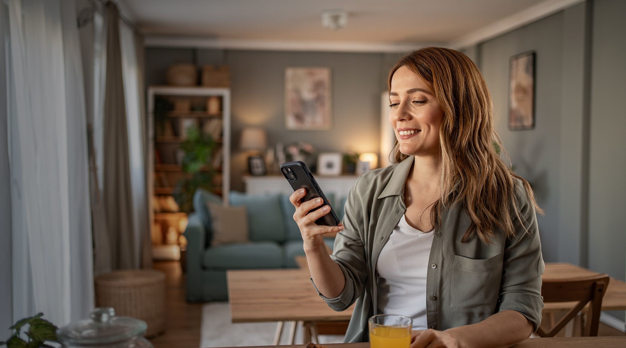 Woman with a smile on her face holding mobile phone in her living room. 