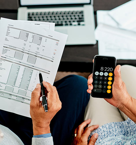 Older couple looking at paperwork and using phone calculator.